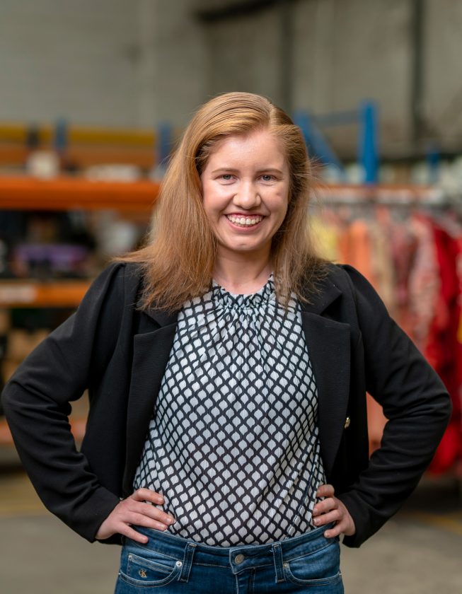 Kayla wearing black suit jacket with hands on hips, smiling at camera.