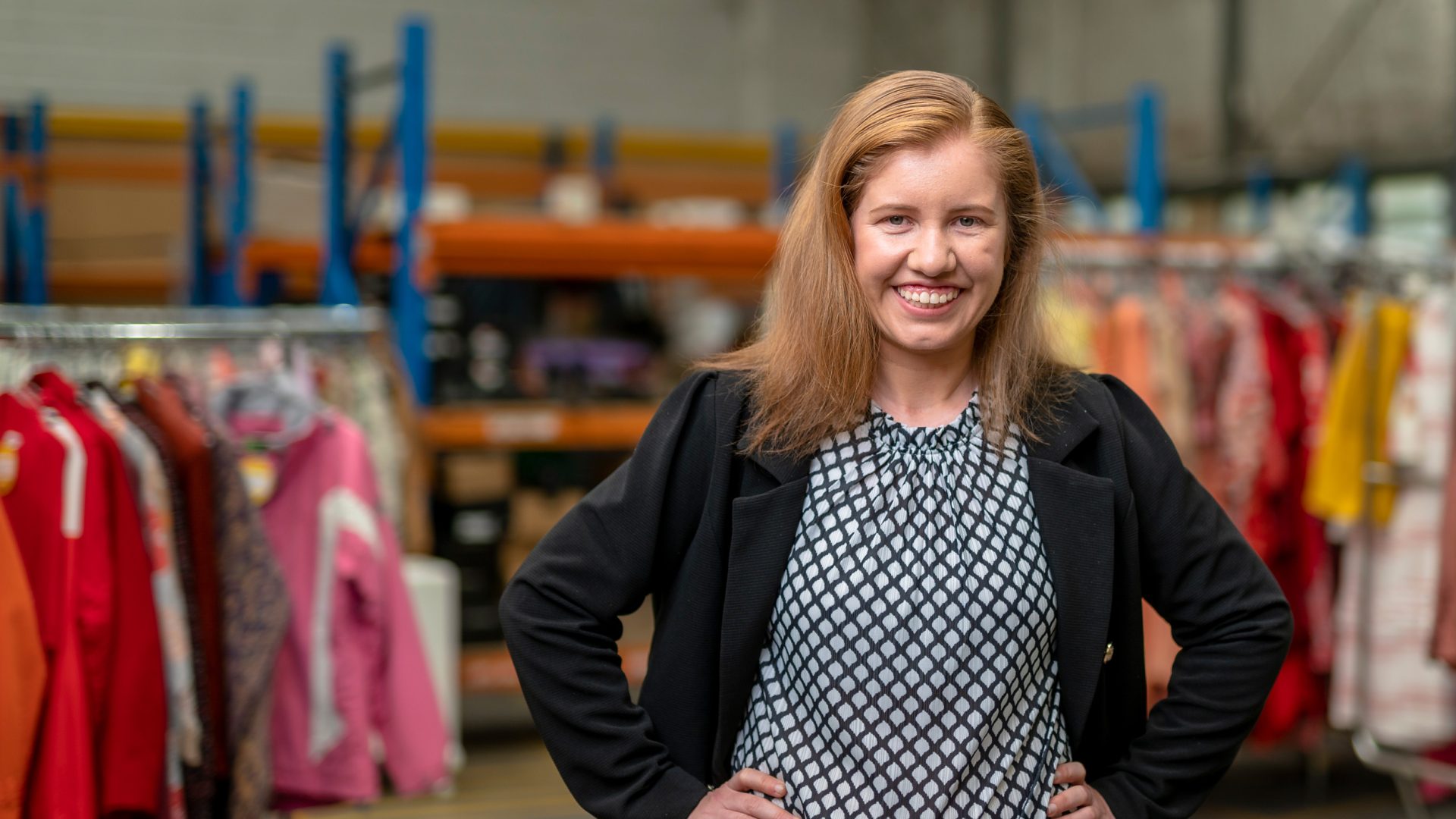 Good Sammy Enterprises employee wearing black suit jacket with hands on hips, smiling at camera.