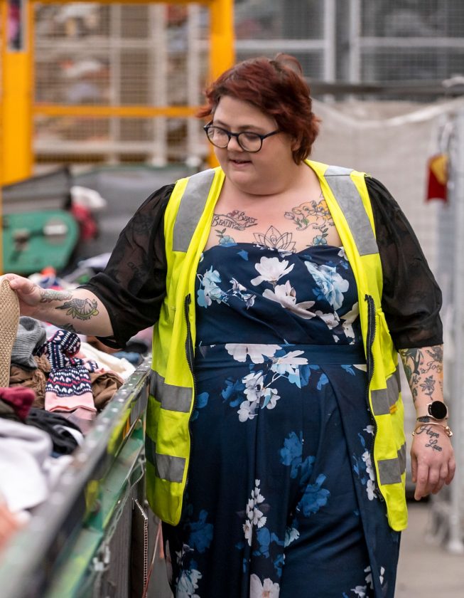 Karen walking alongside a conveyor belot of pre-loved donations, inspecting items.