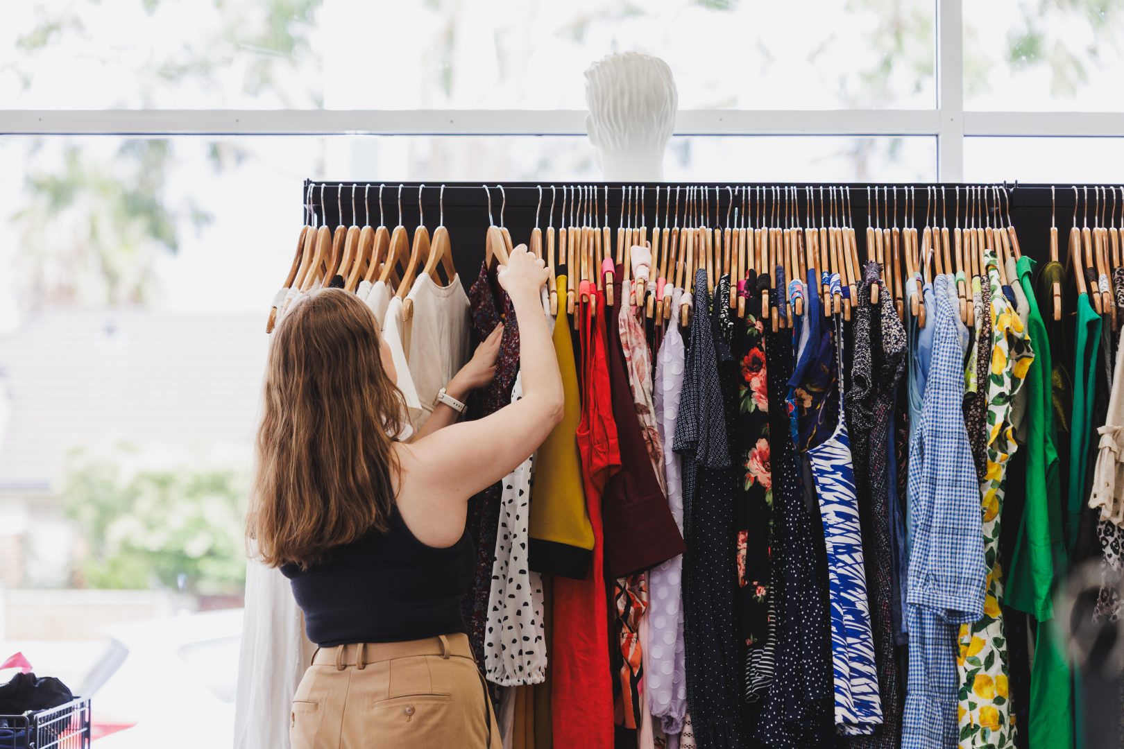 A woman with her back to the camera looking through a rack of brightly coloured summer dresses.